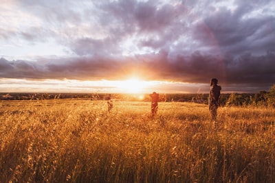 日落时，三个人站在白云下的棕色草地上